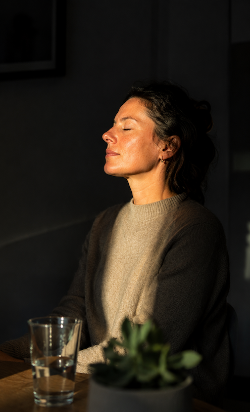 Mujer con los ojos cerrados recibiendo luz natural, símbolo de calma, bienestar emocional y conexión interior en psicología.